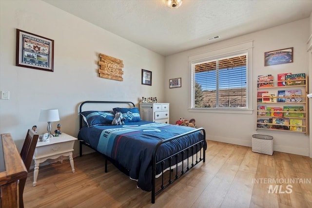 bedroom featuring visible vents, a textured ceiling, baseboards, and hardwood / wood-style floors