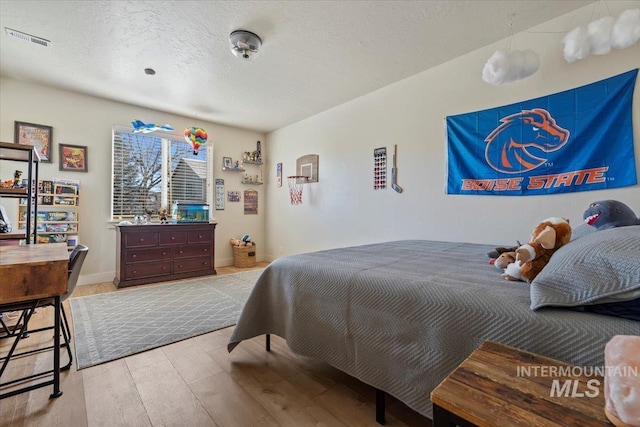 bedroom with baseboards, wood finished floors, visible vents, and a textured ceiling