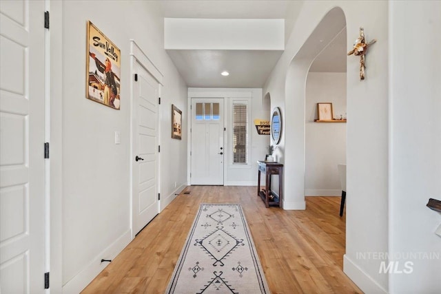 entrance foyer featuring arched walkways, recessed lighting, baseboards, and light wood-style floors