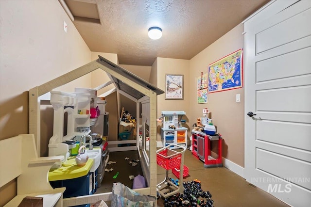 game room with baseboards, concrete flooring, and a textured ceiling