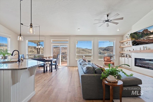 living room featuring a glass covered fireplace, light wood-style flooring, plenty of natural light, and lofted ceiling