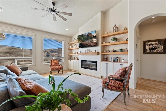 living area featuring light wood finished floors, ceiling fan, lofted ceiling, arched walkways, and a textured ceiling