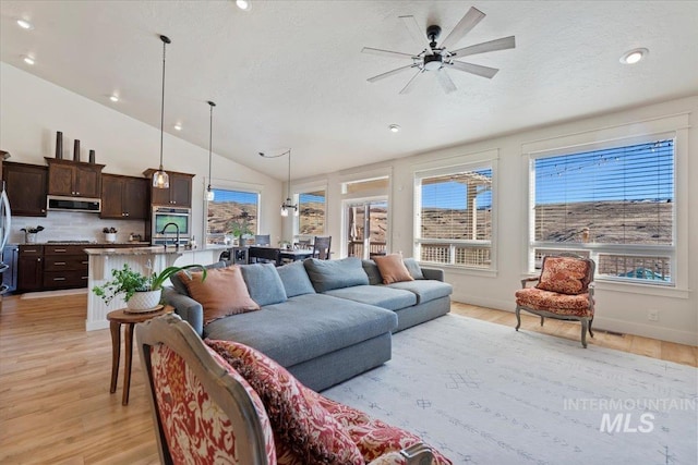 living room with vaulted ceiling, a ceiling fan, light wood finished floors, and a healthy amount of sunlight