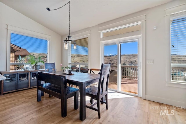 dining space with a notable chandelier, light wood-style flooring, baseboards, and vaulted ceiling