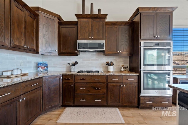 kitchen featuring light stone counters, tasteful backsplash, appliances with stainless steel finishes, and dark brown cabinetry