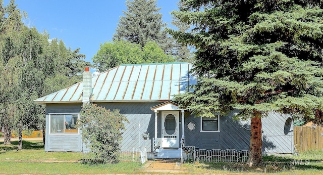 view of front of property featuring entry steps, a chimney, metal roof, a standing seam roof, and fence