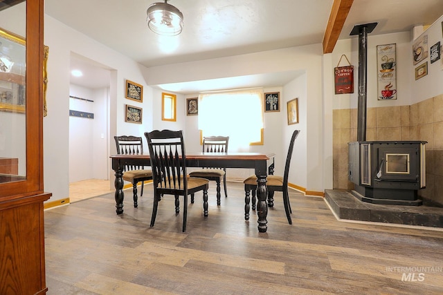 dining area featuring beamed ceiling, wood finished floors, a wood stove, and baseboards