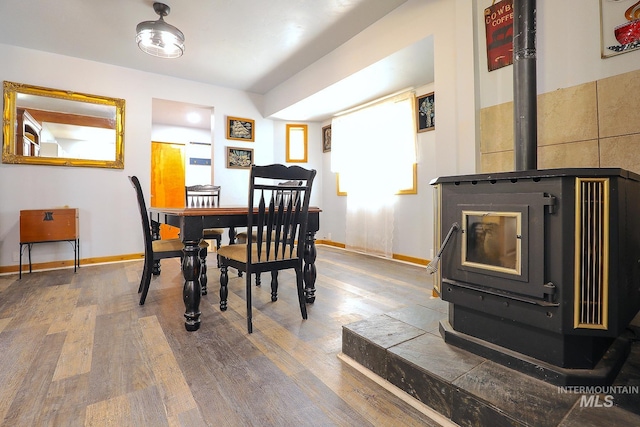 dining space with wood finished floors, a wood stove, and baseboards