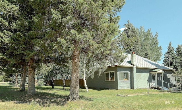 view of home's exterior featuring entry steps, a chimney, metal roof, and a lawn