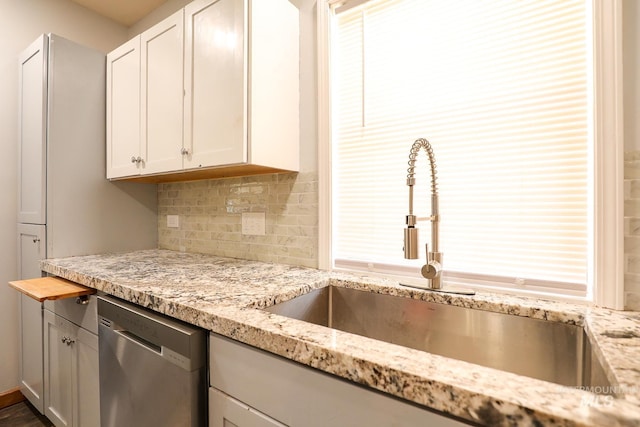 kitchen featuring light stone countertops, a sink, white cabinets, stainless steel dishwasher, and decorative backsplash