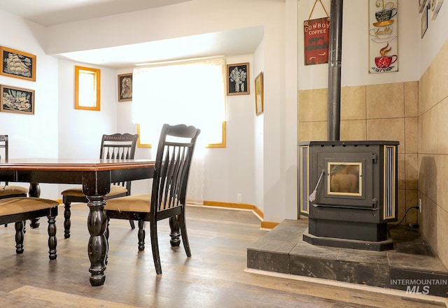 dining space featuring a wood stove, baseboards, and wood finished floors