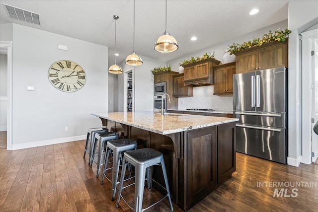 9968 Moon Shadow Ct, Middleton, ID 83644 - kitchen featuring appliances with stainless steel finishes, dark wood-type flooring, light stone countertops, a center island with sink, and backsplash