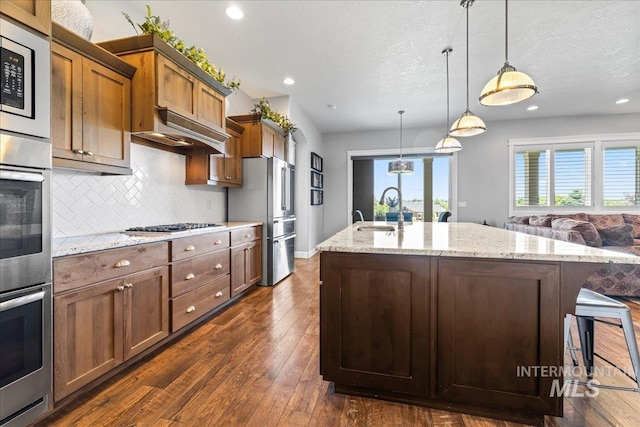 9968 Moon Shadow Ct, Middleton, ID 83644 - kitchen with stainless steel appliances, backsplash, light stone countertops, dark wood-style floors, and an island with sink