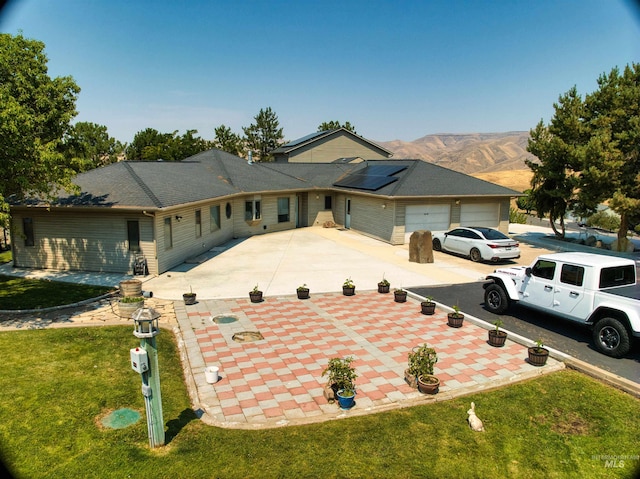 ranch-style house with a garage, solar panels, a mountain view, and a front yard