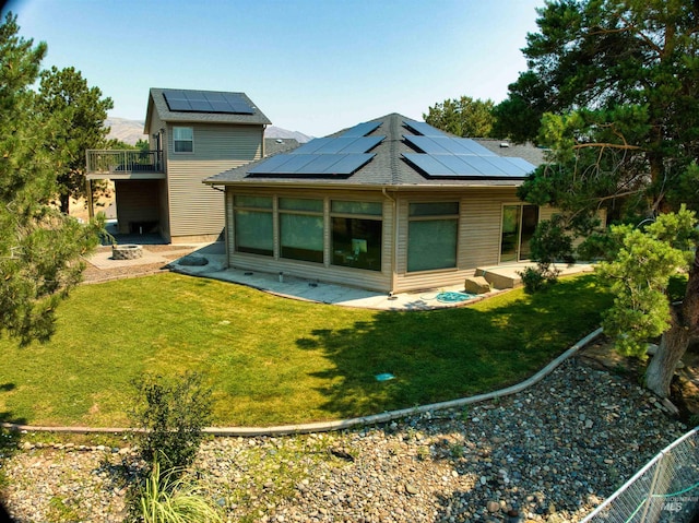 back of house with a balcony, a lawn, and solar panels