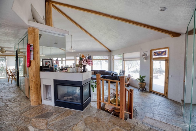 interior space with ceiling fan, lofted ceiling with beams, a multi sided fireplace, and a textured ceiling