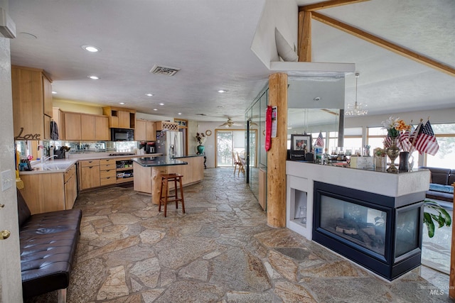 kitchen with hanging light fixtures, backsplash, a multi sided fireplace, stainless steel fridge, and a kitchen breakfast bar