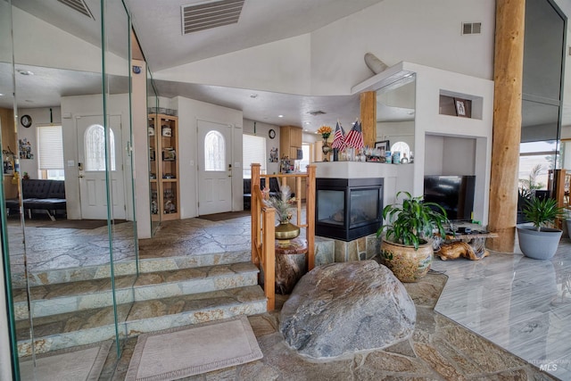 tiled foyer with high vaulted ceiling and a multi sided fireplace