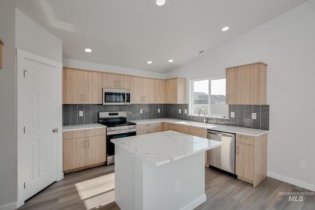 kitchen with stainless steel appliances, light brown cabinetry, a center island, and sink