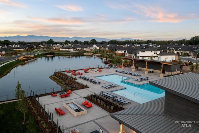 pool at dusk featuring a water and mountain view, an outdoor fire pit, and a patio area