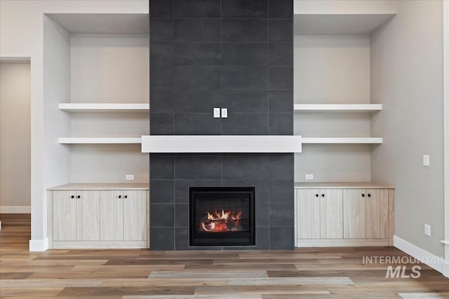 unfurnished living room with built in features, light hardwood / wood-style flooring, and a tile fireplace