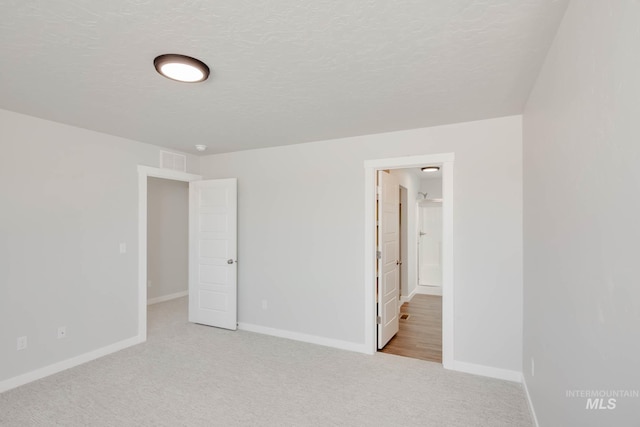 unfurnished bedroom with a textured ceiling, light carpet, and ensuite bathroom