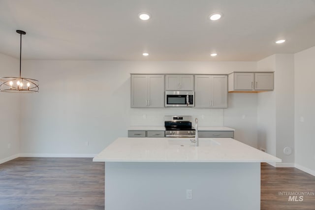 kitchen with light stone countertops, stainless steel appliances, a notable chandelier, dark hardwood / wood-style floors, and a kitchen island with sink