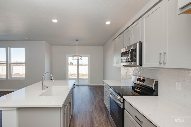 kitchen featuring a kitchen island with sink, stainless steel appliances, sink, light stone countertops, and dark wood-type flooring