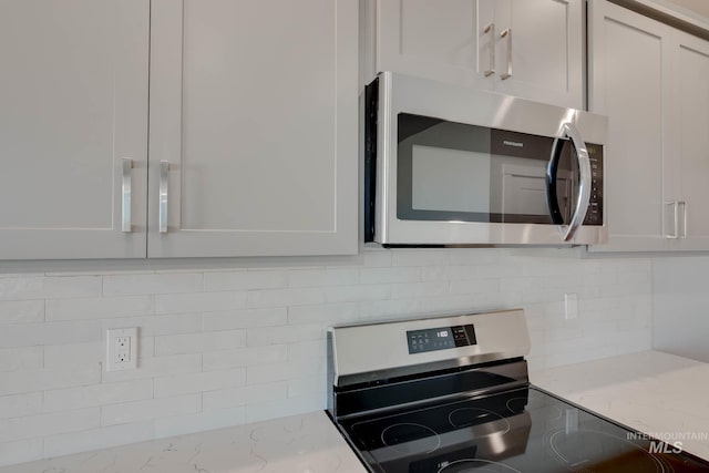 kitchen with stainless steel appliances, light stone counters, and white cabinetry