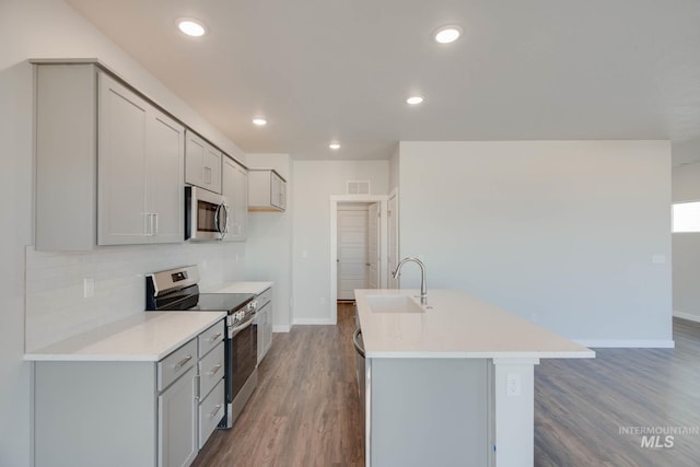 kitchen with gray cabinetry, wood-type flooring, appliances with stainless steel finishes, a kitchen island with sink, and sink