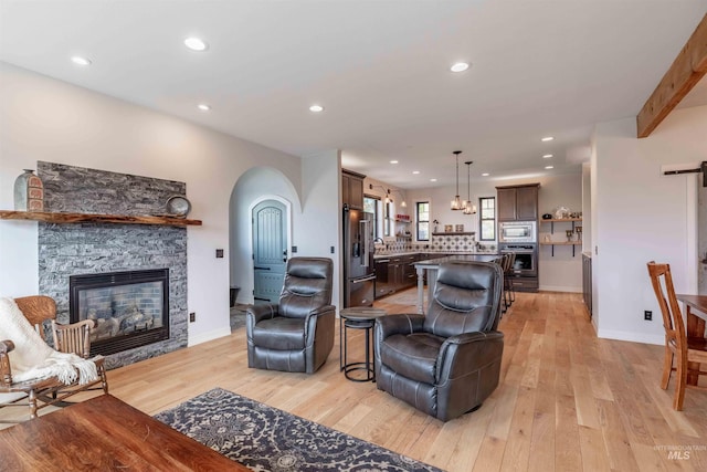 living room featuring baseboards, arched walkways, a fireplace, light wood finished floors, and recessed lighting
