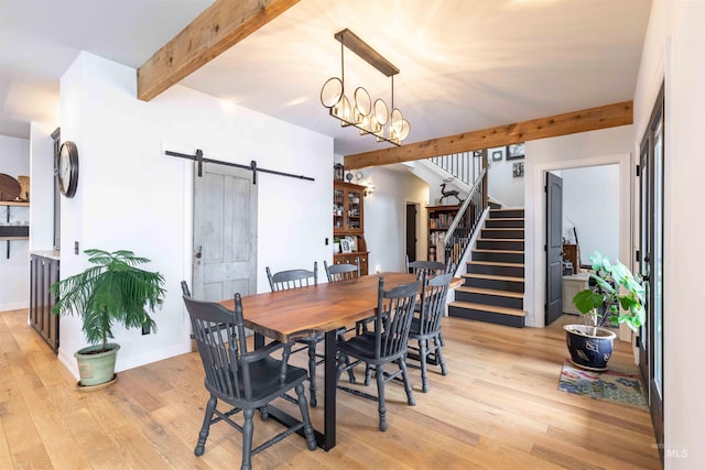 dining space featuring beam ceiling, light wood-type flooring, a barn door, and stairs