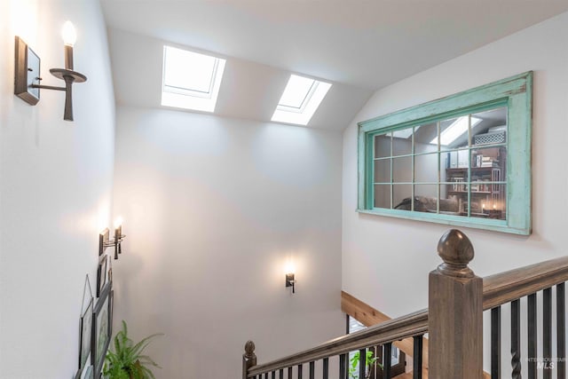 hall with vaulted ceiling with skylight and an upstairs landing