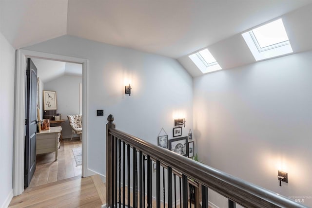 hallway with light wood finished floors, an upstairs landing, and lofted ceiling with skylight