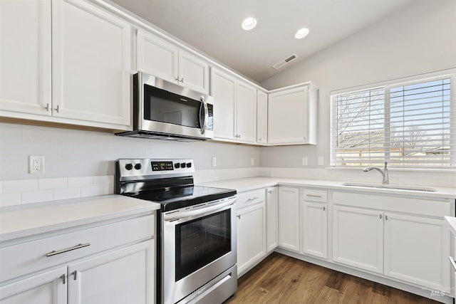 kitchen with visible vents, a sink, stainless steel appliances, white cabinets, and vaulted ceiling