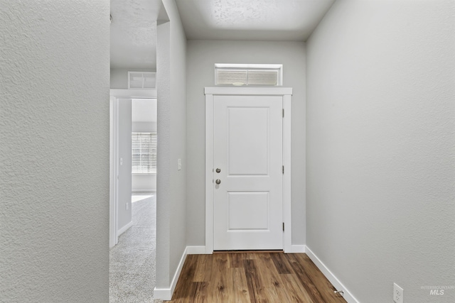 doorway with dark wood finished floors, a textured wall, and baseboards