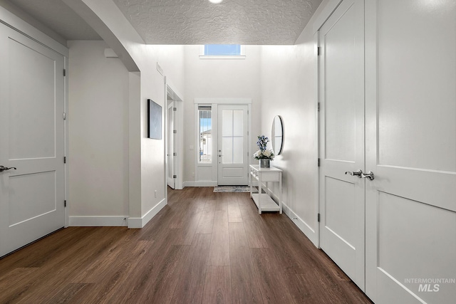 entryway featuring baseboards, dark wood-style floors, arched walkways, and a textured ceiling