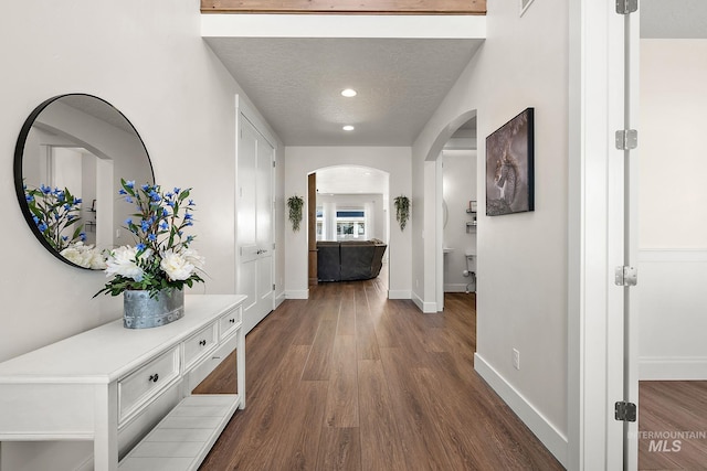 hall with baseboards, recessed lighting, arched walkways, dark wood-style floors, and a textured ceiling