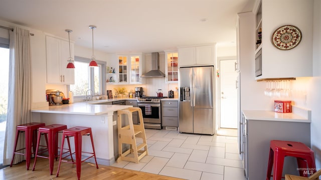 kitchen with tasteful backsplash, appliances with stainless steel finishes, glass insert cabinets, wall chimney range hood, and a peninsula