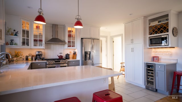 kitchen with wall chimney exhaust hood, wine cooler, stainless steel appliances, light countertops, and a sink