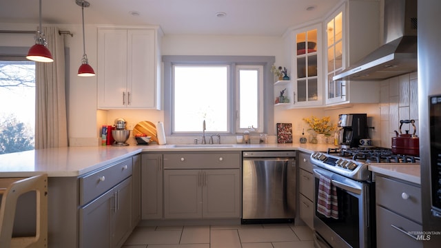 kitchen with stainless steel appliances, light countertops, gray cabinetry, a sink, and wall chimney range hood