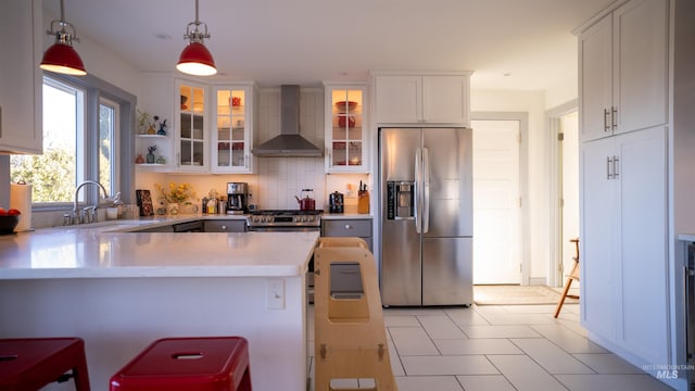 kitchen featuring light countertops, appliances with stainless steel finishes, white cabinetry, wall chimney range hood, and a peninsula