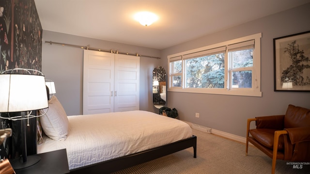 carpeted bedroom with a barn door and baseboards