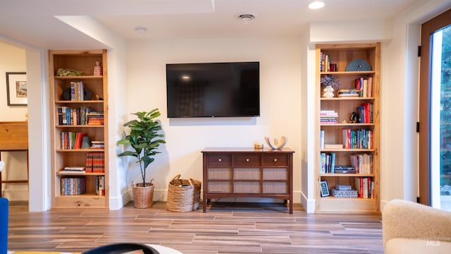 living room featuring built in shelves, wood finish floors, baseboards, and recessed lighting