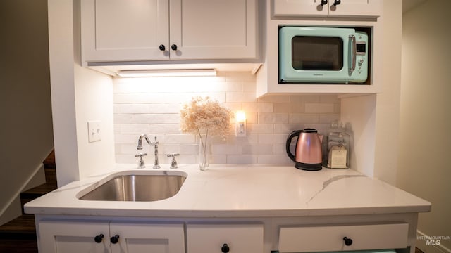 kitchen with white cabinets, white microwave, light stone counters, a sink, and backsplash