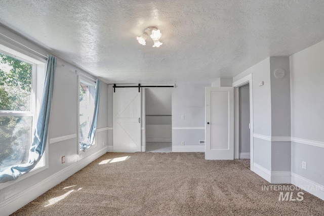712 Yakima Ave, Filer, ID 83328 - unfurnished bedroom featuring a barn door, a textured ceiling, carpet floors, and baseboards