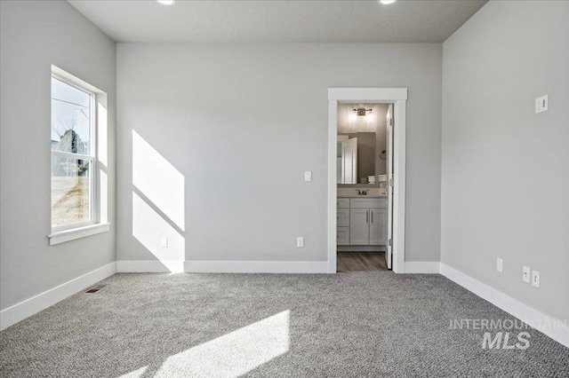 unfurnished bedroom featuring carpet, visible vents, baseboards, a sink, and ensuite bathroom