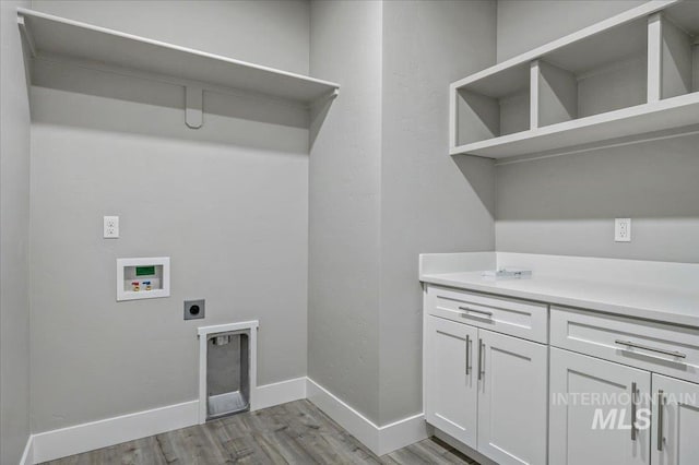 washroom featuring electric dryer hookup, light wood-type flooring, washer hookup, cabinet space, and baseboards