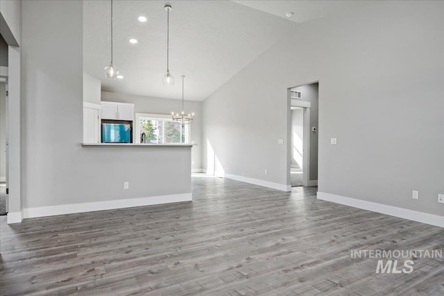 unfurnished living room with baseboards, lofted ceiling, a notable chandelier, and wood finished floors