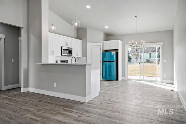 kitchen featuring white cabinetry, stainless steel microwave, freestanding refrigerator, and a chandelier
